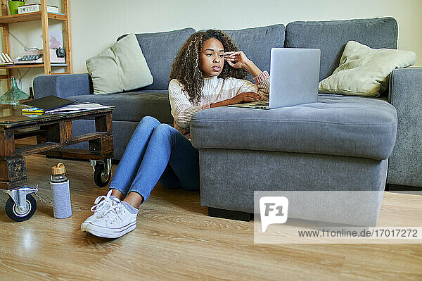 Junge Afro-Frau  die einen Laptop benutzt  während sie zu Hause im Wohnzimmer auf dem Boden sitzt