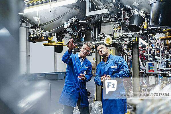 Mature male technicians in overalls examining machine part in factory
