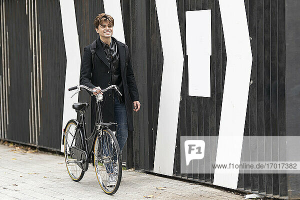 Lächelnder gut aussehender Mann  der auf dem Fußweg an der Mauer Fahrrad fährt