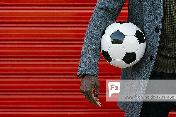 Mann hält Fußball  während er gegen eine rote Wand steht
