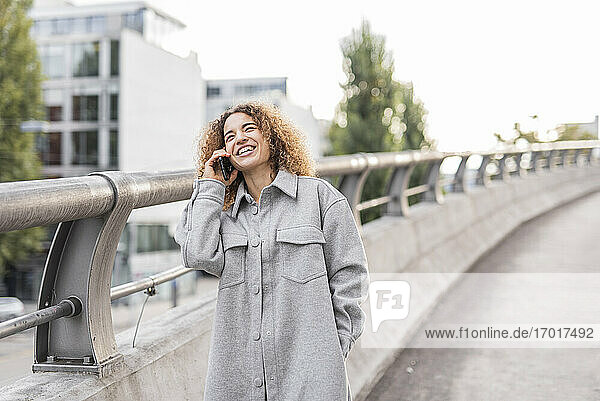 Fröhliche junge Afro-Frau  die auf einer Brücke in der Stadt steht und mit ihrem Handy spricht