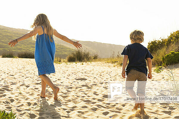 Brother and sister playing while walking on sand
