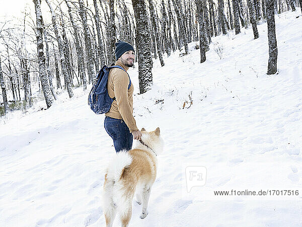 Smiling young man looking away while standing with akita dog in snow covered land