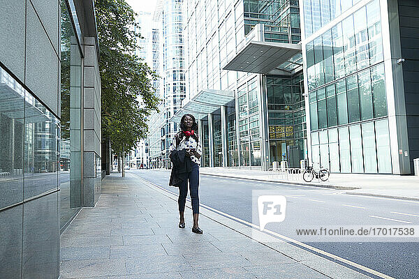 Geschäftsfrau mit Kopfhörern und Mobiltelefon  die einen Blazer in der Hand hält  während sie auf einem Fußweg geht