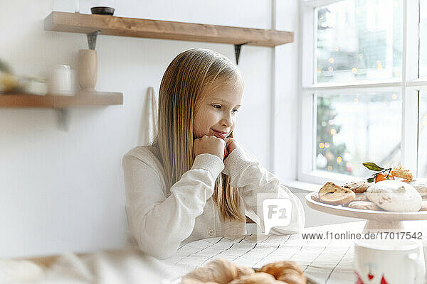 Lächelndes Mädchen betrachtet Kekse auf dem Tisch in der Küche