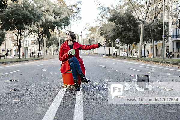 Junge Frau in Winterjacke mit Kaffeetasse wirft zerknülltes Papier aus dem Mülleimer auf die Straße
