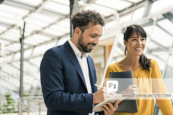 Lächelnder männlicher Kollege  der ein digitales Tablet benutzt  neben einer Unternehmerin im Büro