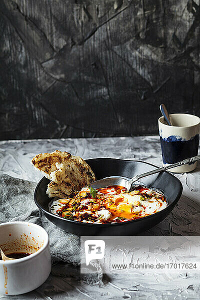 Frühstück mit Joghurt und würziger Paprikabutter auf pochierten Eiern in einer Schale bei einer Kaffeetasse auf dem Tisch