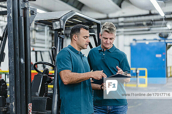Male colleagues discussing over document while working in factory