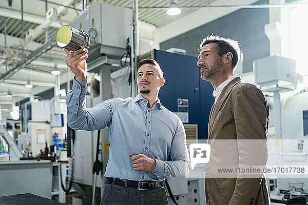 Businessman with male colleague discussing over machine part in industry
