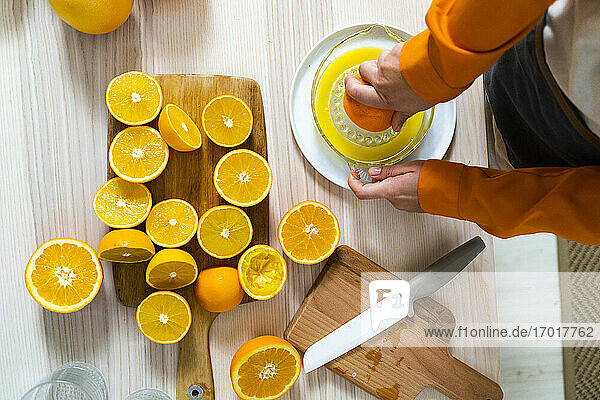 Frau bereitet Orangensaft in einer Saftpresse zu  während sie zu Hause am Tisch steht