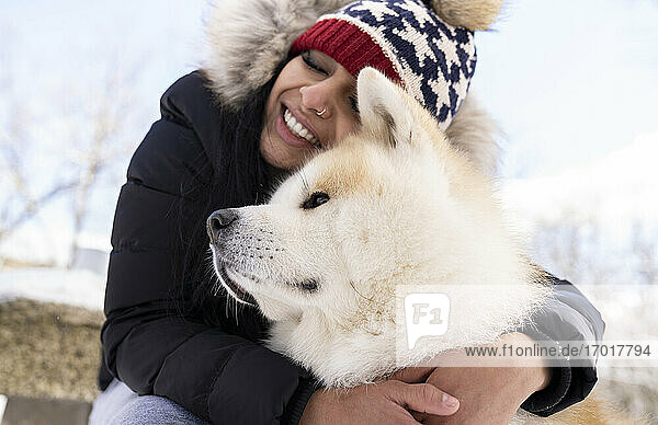 Glückliche Frau mit geschlossenen Augen umarmt Hund im Winter