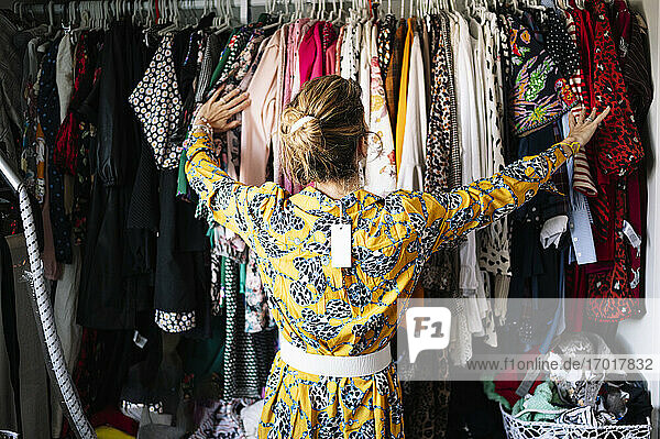 Modische blonde Frau im neuen gelben Kleid wählt aus Kleiderständer in der Wohnung