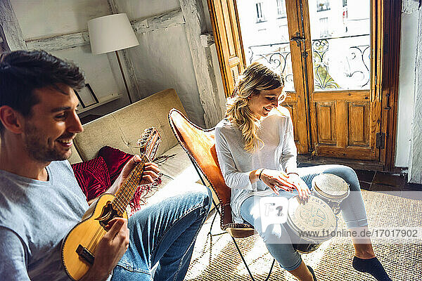 Happy young couple playing duet with drums and guitar in living room at home