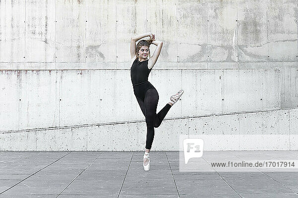 Ballerina in black leotard dancing in front of concrete wall