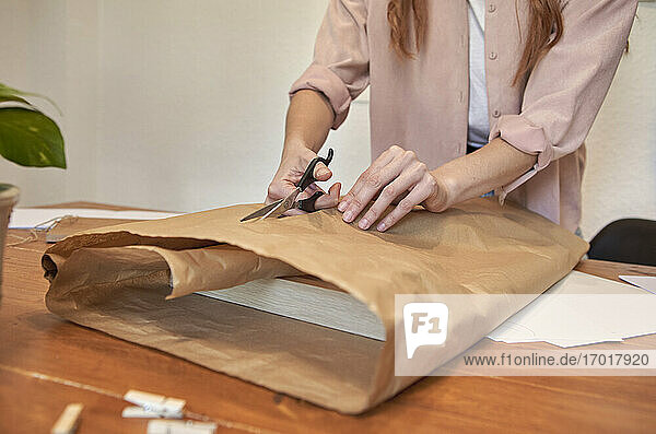 Künstlerin schneidet braunes Papier  während sie am Schreibtisch im Wohnzimmer ein Paket vorbereitet