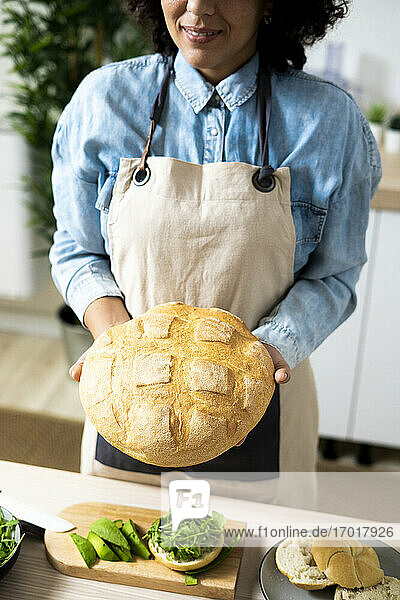 Mittelteil einer jungen Frau  die einen frisch gebackenen Laib Brot hält
