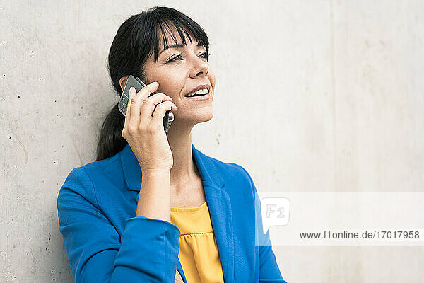 Reife Geschäftsfrau  die mit ihrem Smartphone an der Wand im Büro spricht