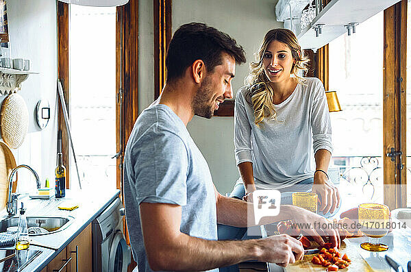 Young man preparing food and talking with girlfriend in kitchen at home
