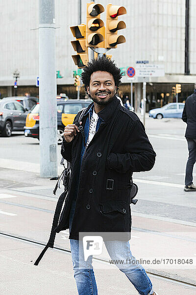 Smiling man with afro hair looking away while walking on street in city