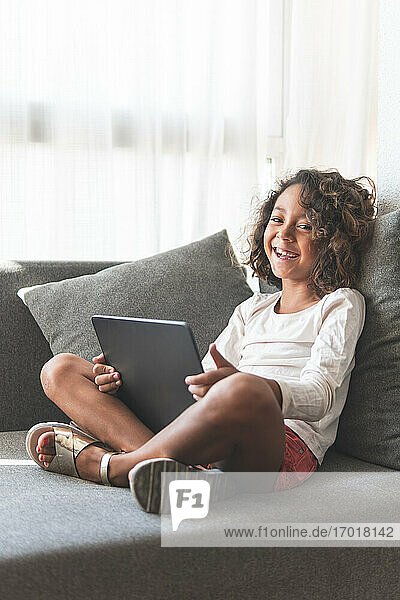 Porträt eines kleinen Mädchens lächelnd auf dem Sofa mit digitalem Tablet in den Händen