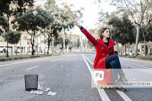 Junge Frau wirft zerknülltes Papier in den Mülleimer  während sie auf der Straße sitzt