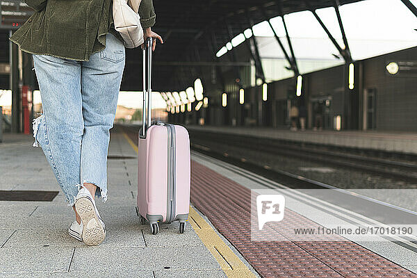 Legs of young woman with suitcase walking on railroad station platform