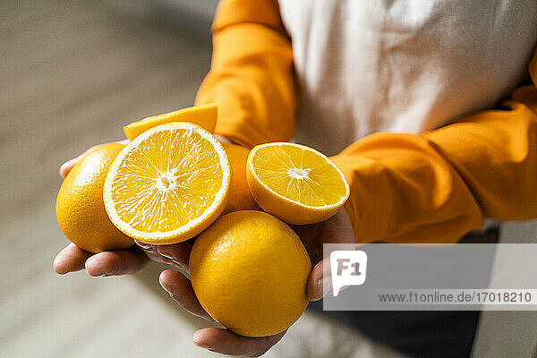Frau hält Orange und Orangenscheibe in der Hand  während sie zu Hause steht