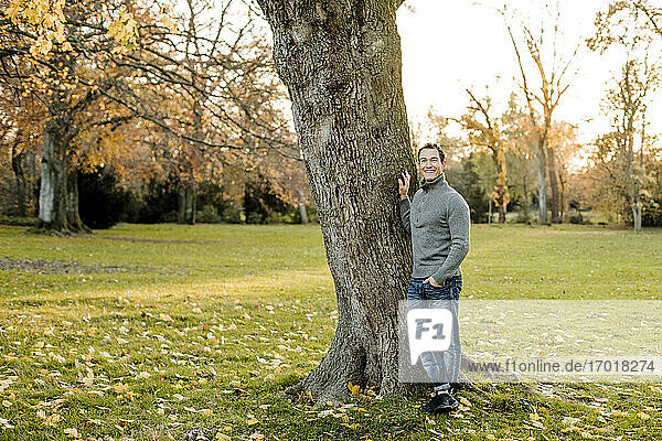 Lächelnder Mann an einem Baumstamm in einem öffentlichen Park im Herbst