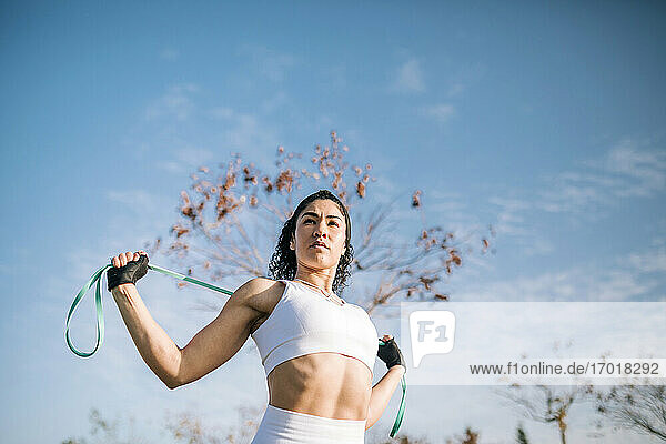 Selbstbewusste Sportlerin mit Widerstandsband gegen den Himmel an einem sonnigen Tag