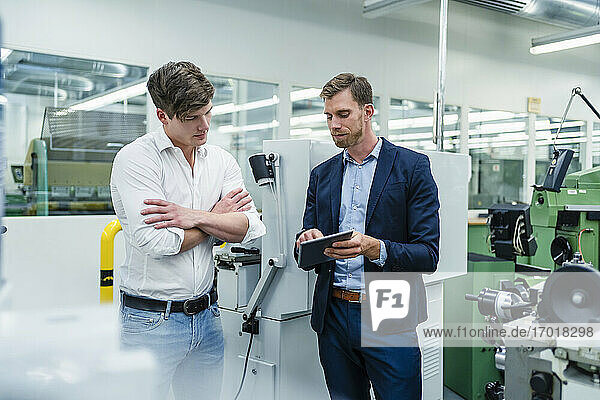 Businessman discussing with male coworker over digital tablet in factory