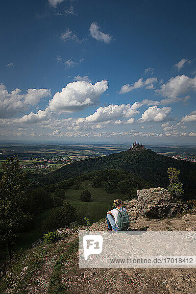 Weibliche Forscherin bewundert den Blick auf die Burg Hohenzollern  während sie auf einem Berg auf der Schwäbischen Alb sitzt  Deutschland
