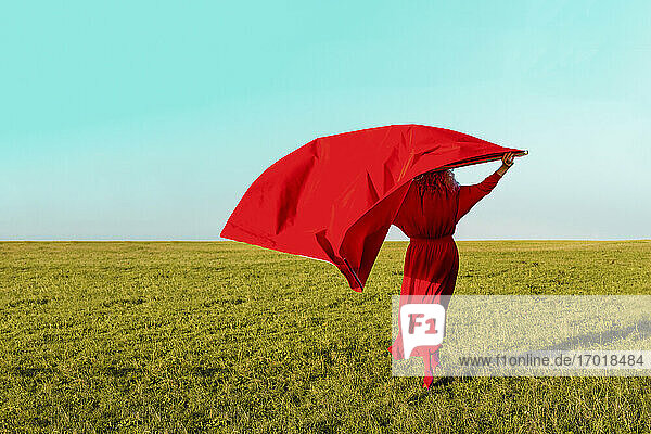 Senior woman with red fabric while standing on grass during sunny day