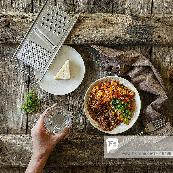 Schüssel mit vegetarischen Spaghetti Bolognese und Hand einer Frau  die ein Glas Wasser hält
