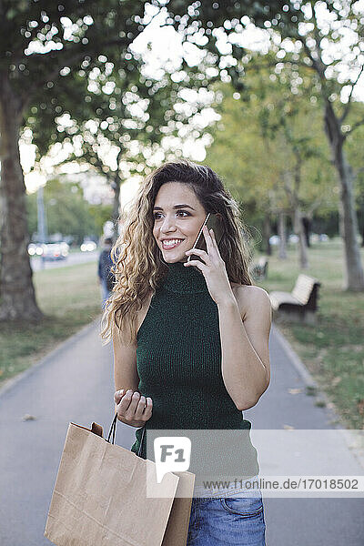 Lächelnde Frau  die wegschaut  während sie in einem öffentlichen Park telefoniert