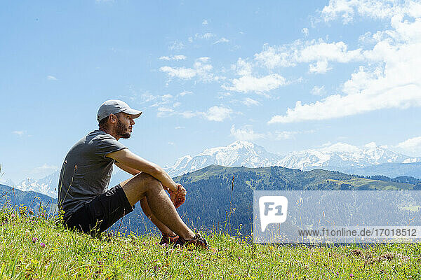 Erwachsener Mann  der über Gras am Col des Aravis  Haute-Savoie  Frankreich  sitzt und nachdenkt