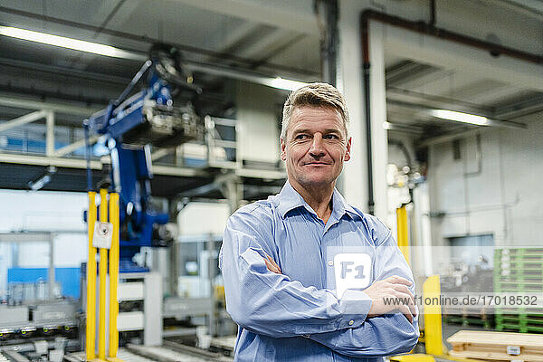 Smiling supervisor with arms crossed looking away in industry