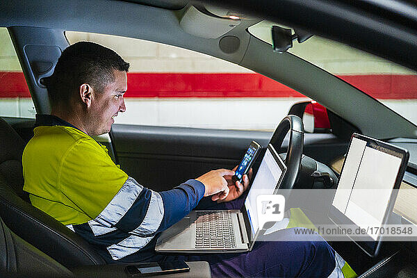 Smiling male programmer working on mobile phone in electric car