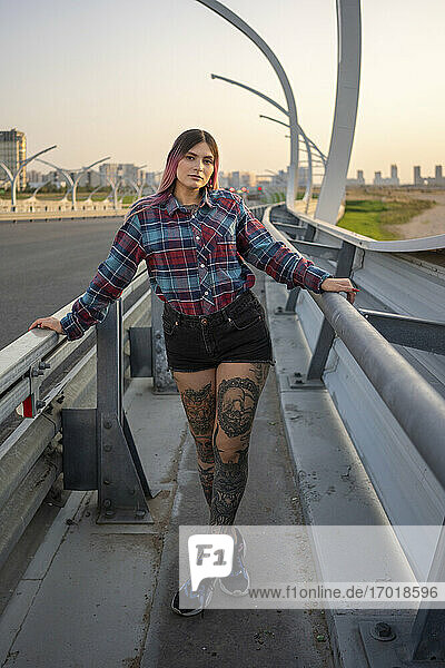 Junge Frau mit Tattoo auf einer Brücke am Straßenrand stehend