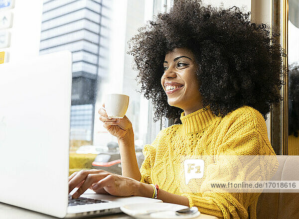 Lächelnde Frau mit Kaffeetasse und Laptop in einem Café sitzend