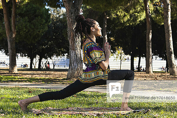 Lächelnde junge Frau übt Yoga im Park an einem sonnigen Tag