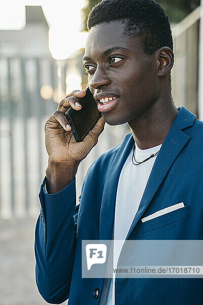 Young businessman in blazer talking on mobile phone call outdoors
