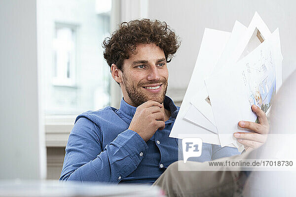 Lächelnder Geschäftsmann mit Hand am Kinn beim Lesen eines Dokuments im Büro
