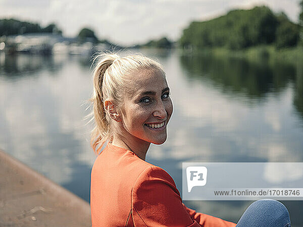 Lächelnde Geschäftsfrau sitzt am Seeufer an einem sonnigen Tag