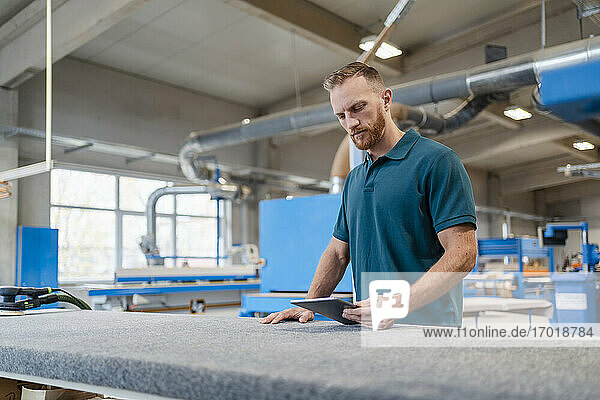 Porträt eines Schreiners in einer Produktionshalle mit einem digitalen Tablet in der Hand