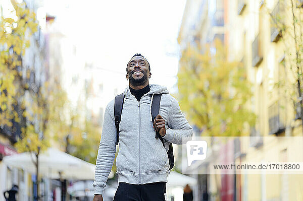 Junger Mann mit Rucksack lächelnd beim Spaziergang in der Stadt