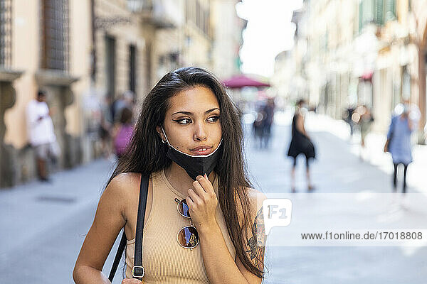 Frau entfernt Gesichtsmaske  während sie auf der Straße in der Stadt steht