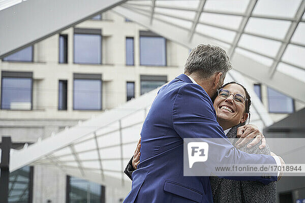 Senior businessman hugging cheerful businesswoman while greeting in city