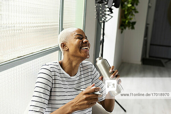 Lachende Frau  die in einem Büro aus einer Flasche trinkt