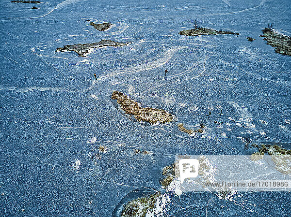 Luftaufnahme von zwei Fischern  die auf der Oberfläche eines zugefrorenen Sees spazieren gehen